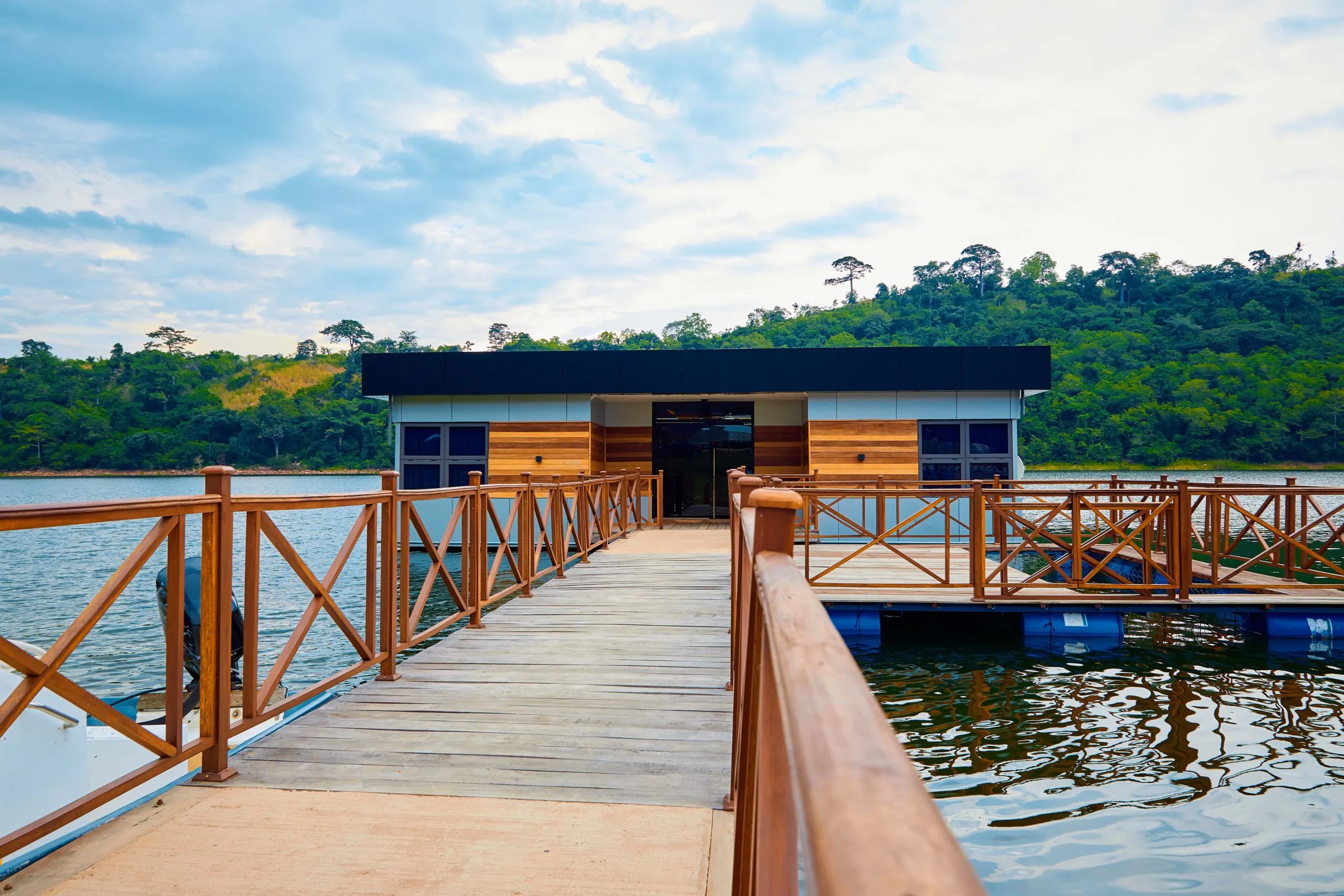 The Float resort: a wooden walkway leading to a modern floating structure on Lake Volta, surrounded by green hills.